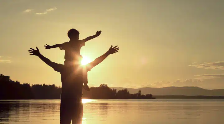 A man standing in front of a sunset over a body of water